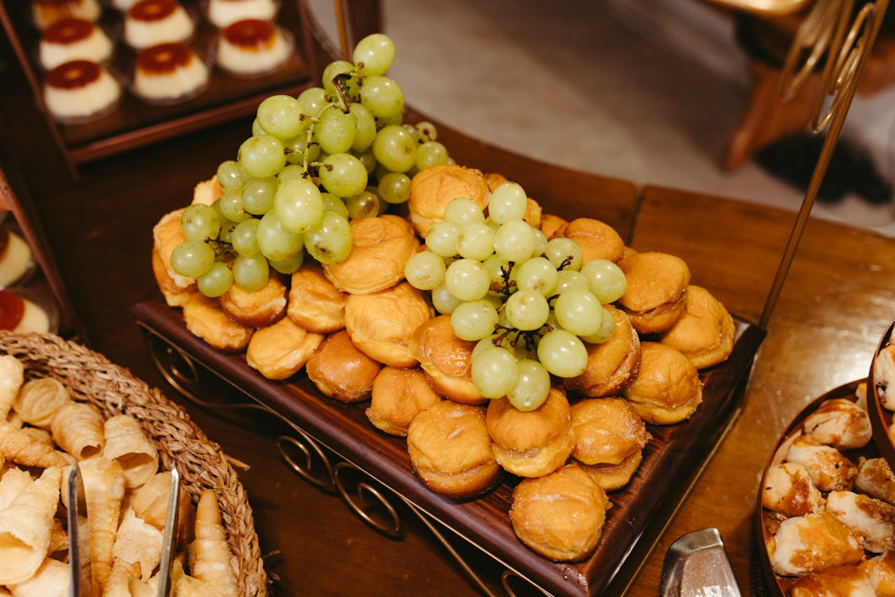 A beautifully arranged dessert tray topped with green grapes, showcasing a variety of pastries.